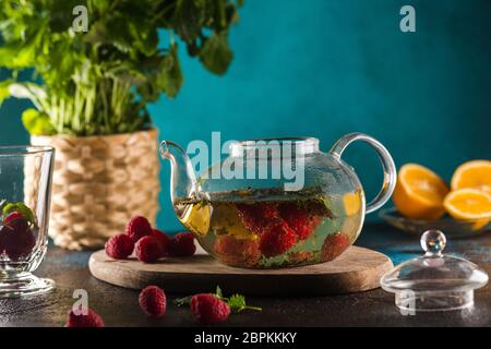 teapot with raspberry tea mint leaves and lemon on blue Stock Photo