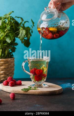 raspberry and mint tea pouring in cup on wooden board blue wall Stock Photo