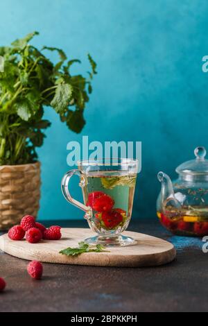 glass cup with raspberry tea mint leaves and lemon on blue Stock Photo