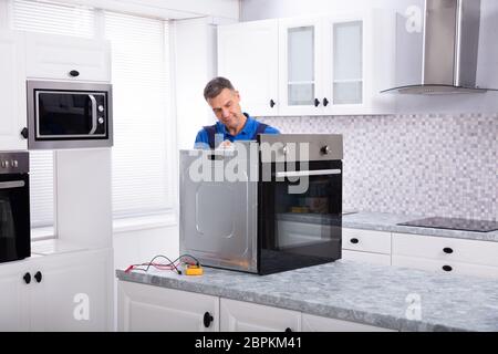 Mature Male Technician Repairing Oven On Kitchen Worktop Stock Photo