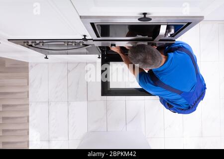 Mature Technician In Overall Repairing Oven In Kitchen Stock Photo