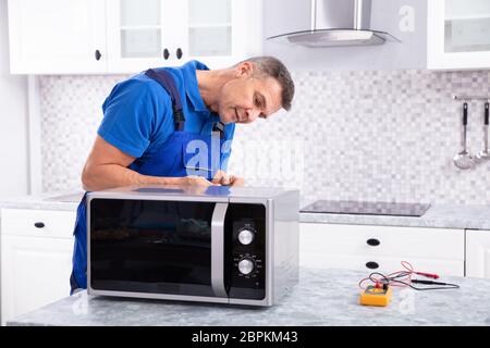 Side View Of Mature Man Repairing Microwave Oven In Kitchen Stock Photo