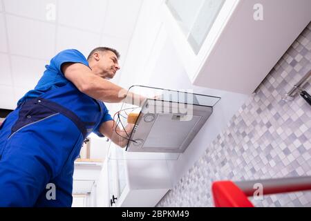 Elevated View Of Male Technician Checking Extractor Filter With Digital Multimeter In Kitchen Stock Photo