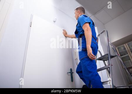 Low Angle View Of Man Standing On Step Ladder Testing Security System Door Sensor Stock Photo