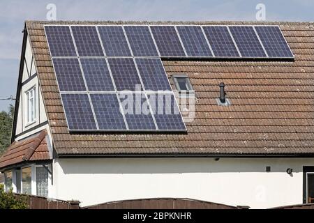 Solar Panels in sunshine installed on south facing roof on sunny blue sky day detached house alongside an existing roof light panel Essex England UK Stock Photo