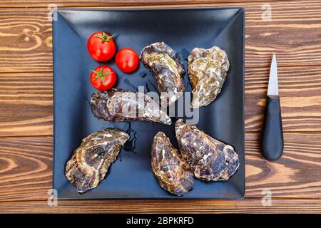 Fresh oysters on a black plate on a wooden table Stock Photo