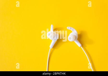 White headphones with a wire on a yellow background. The concept of gadgets. Stock Photo
