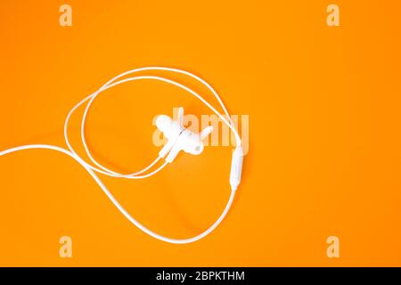 White headphones with a wire on a orange background. The concept of gadgets. Stock Photo