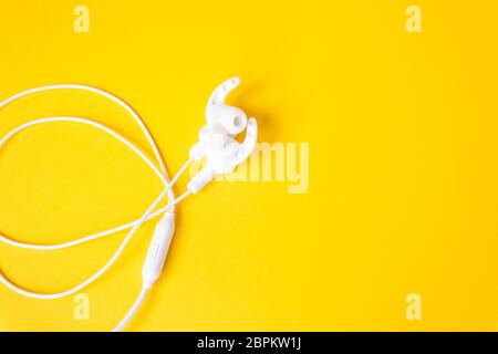 White headphones with a wire on a yellow background. The concept of gadgets. Stock Photo