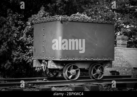 Monochrome, black and white close up of vintage coal truck isolated outdoors on rails, Black Country Living Museum, UK. Vintage mining. Stock Photo