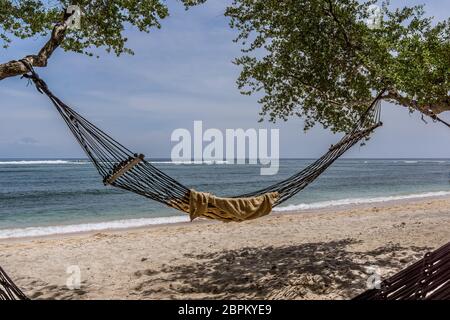 A black hammock and a towel svinging between two trees on the tropical beach, Gili  Trawngan, Indonesia, April 25, 2018 Stock Photo