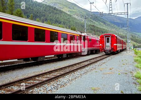 The train pulls up to the station of the old narrow-gauge railway in the valley of the Alpine mountains among the trees in cloudy weather. Stock Photo