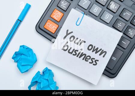 Hand writing in a notebook your own business on a white background with a calculator. Close up. Stock Photo