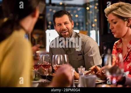 Mid adult man sitting at a restaurant table with some friends and enjoying a meal. Stock Photo