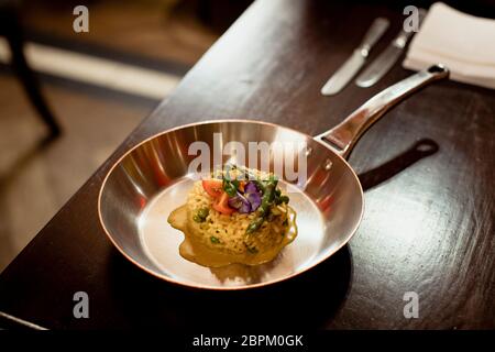 Restaurant style risotto dish presented in a silver frying pan on a wooden table in a restaurant.
