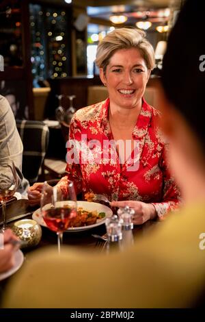 Over the shoulder view of a mature woman talking with her friends during a meal in a restaurant. Stock Photo
