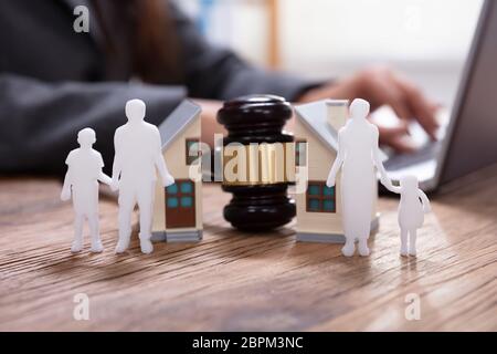 Close-up Of Gavel Between Split Family Figures And House Model With Business Person Using Laptop Stock Photo