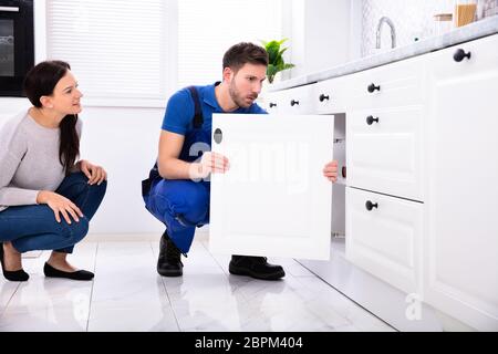 Woman Looking At Male Handyman Installing Cabinet Door In The Kitchen Stock Photo