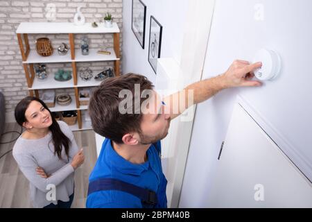 Pretty Woman Standing Near Repairman Installing Smoke Detector On Wall At Home Stock Photo