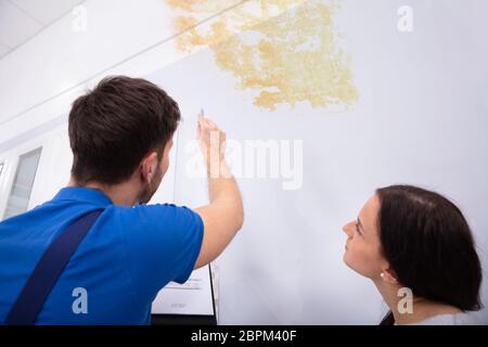 Young Worker Writing On Clipboard With Woman Standing In Kitchen Stock Photo