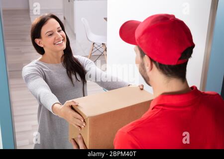 Happy Young Woman Accepting Cardboard Box From Delivery Man Stock Photo