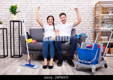 Portrait Of Happy Young Couple With Clenched Fist Sitting On Sofa In Living Room Stock Photo