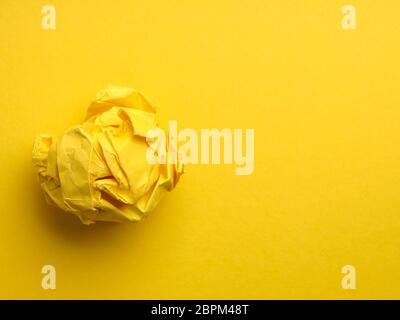Crumpled yellow paper ball on a yellow background with space for text or image, view from above Stock Photo