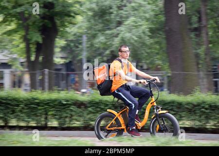 Belgrade, Serbia - May 15, 2020: Young city delivery service courier riding an electric orange bike in city park Stock Photo