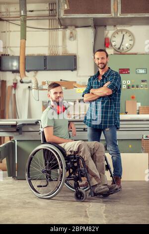 disabled worker in wheelchair in a carpenter's workshop with his colleague Stock Photo