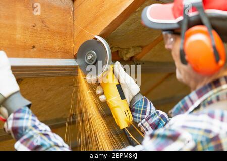 Man fixing metal frame using angle grinder on attic ceiling covered with rock wool Stock Photo