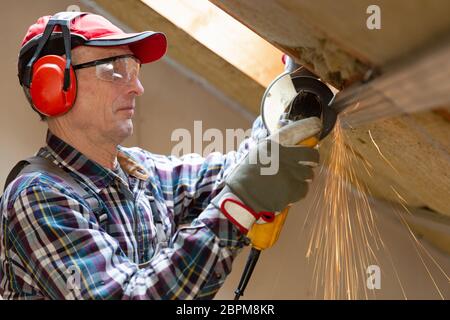 Man fixing metal frame using angle grinder on attic ceiling covered with rock wool Stock Photo