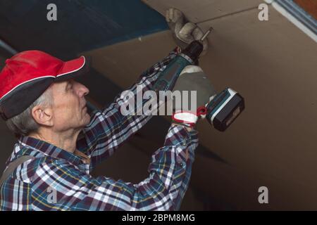 Drywall construction, attic renovation. Man fixing drywall suspended ceiling to metal frame using electrical screwdriver Stock Photo