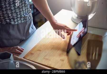 Woman Using Touch Screen on a Digital Tablet In The Kitchen At Home on a Chopping Board Stock Photo