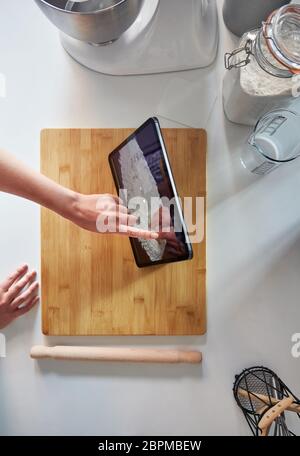Woman Using Touch Screen on a Digital Tablet In The Kitchen At Home on a Chopping Board Stock Photo
