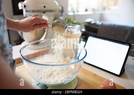 Woman pouring flower into a mixing bowl at home, close in. On digital scales Stock Photo