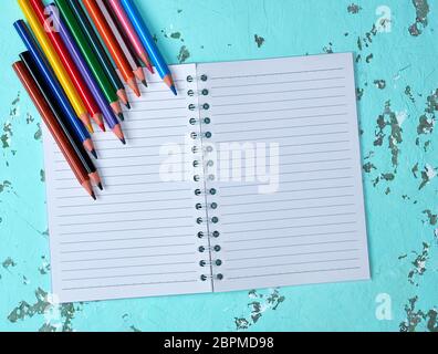 open notebook in a line and multi-colored wooden pencils on a green background Stock Photo