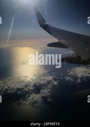 Airplane flight over the Mediterranean Sea at sunrise with view over the wings and cotton candy clouds Stock Photo