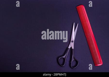 Hairdressing scissors with a red comb on a black background with copy space. Hairdresser tools. Haircut in a beauty salon, barbershop. Stock Photo