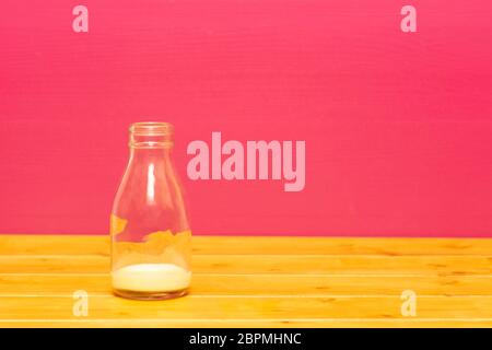 One-third pint glass milk bottle with dregs of banana milkshake, on a wooden table against a pink painted background Stock Photo