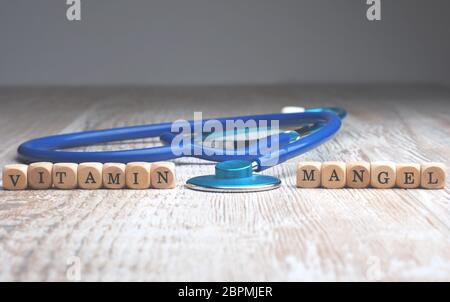The German words vitamin deficiency on small wooden blocks with a stethoscope on a table, health care or medical concept Stock Photo