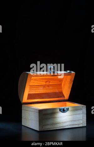 Small wooden chest inside illuminates against a black background with spotlight on the lock. Stock Photo