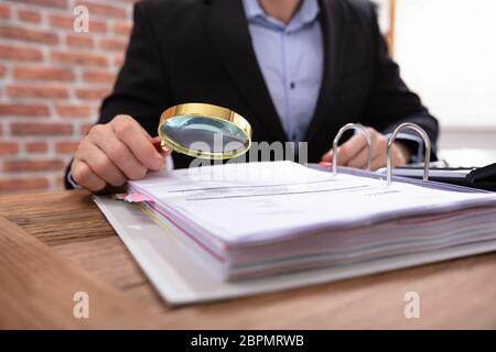 Close-up Of A Businessman's Hand Examining Invoice Through Magnifying Glass On Wooden Desk Stock Photo