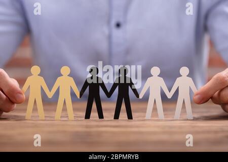 Businessperson's Hand Holding Human Figures Standing In A Row Stock Photo