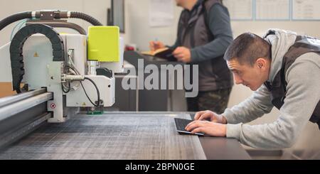 Two printshop worker technicians works on large CNC computer numerical control printing and cutting machine Stock Photo