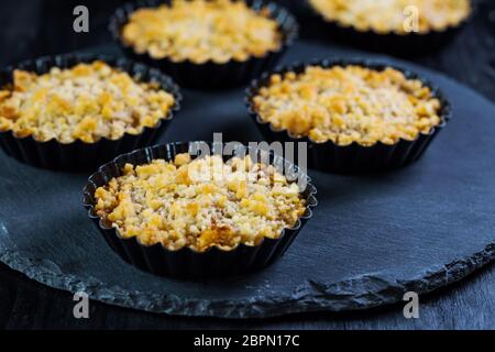 Small and delicious apple pies or apple crumble on black background. Apple tart. Stock Photo