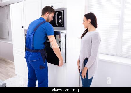 Beautiful Woman Looking At Young Serviceman Installing Oven In Kitchen Stock Photo
