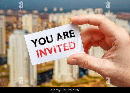 Male hand holds a card with the inscription You Are Invited on a sity background Stock Photo