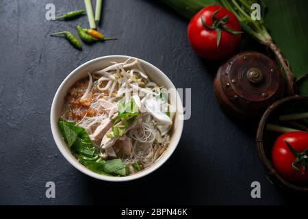 Asian rice noodles soup and chicken in bowl on dark background. Top view flat lay. Stock Photo