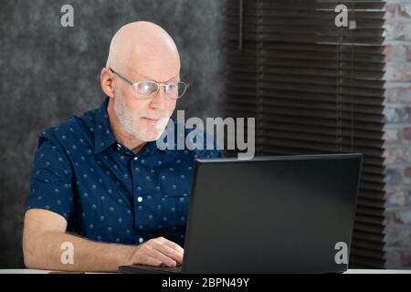 mature man with a white beard and blue shirt using a laptop Stock Photo