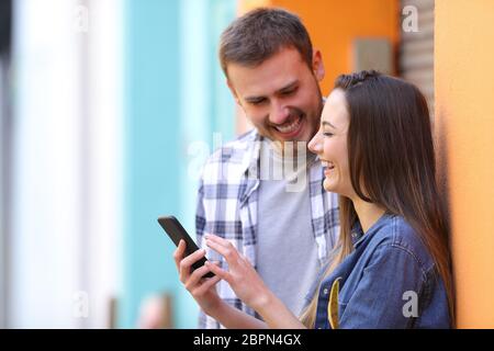 Happy couple laughing browsing smart phone content in the street Stock Photo